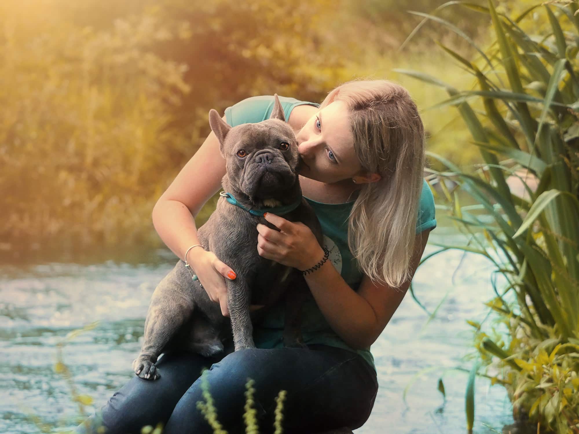 Nadja und Schmugen Nadja sitzt mit ihrer Französischen Bulldogge an einem Bach und gibt ihm einen Kuss.